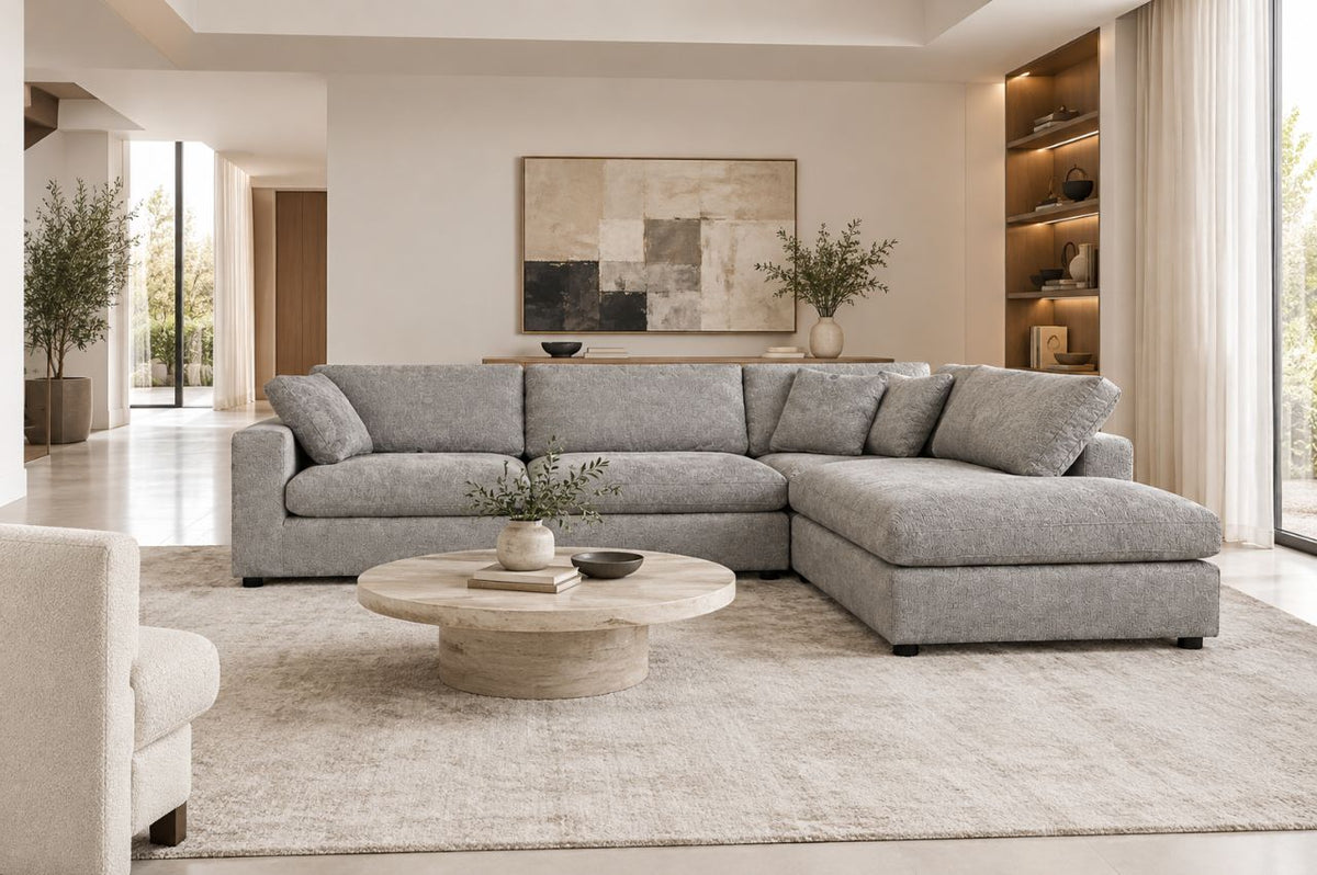 Premium modern living room featuring a large light-gray L-shaped sectional sofa, round stone coffee table, neutral textured rug, and elegant contemporary décor in a bright white interior.